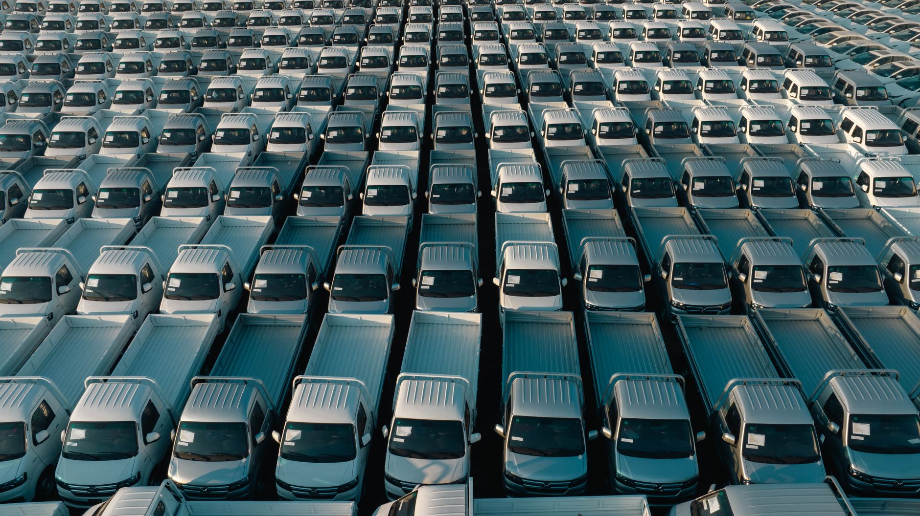 Overhead shot of a large collection of white pickup trucks parked in neat rows, emphasizing industrial scale.