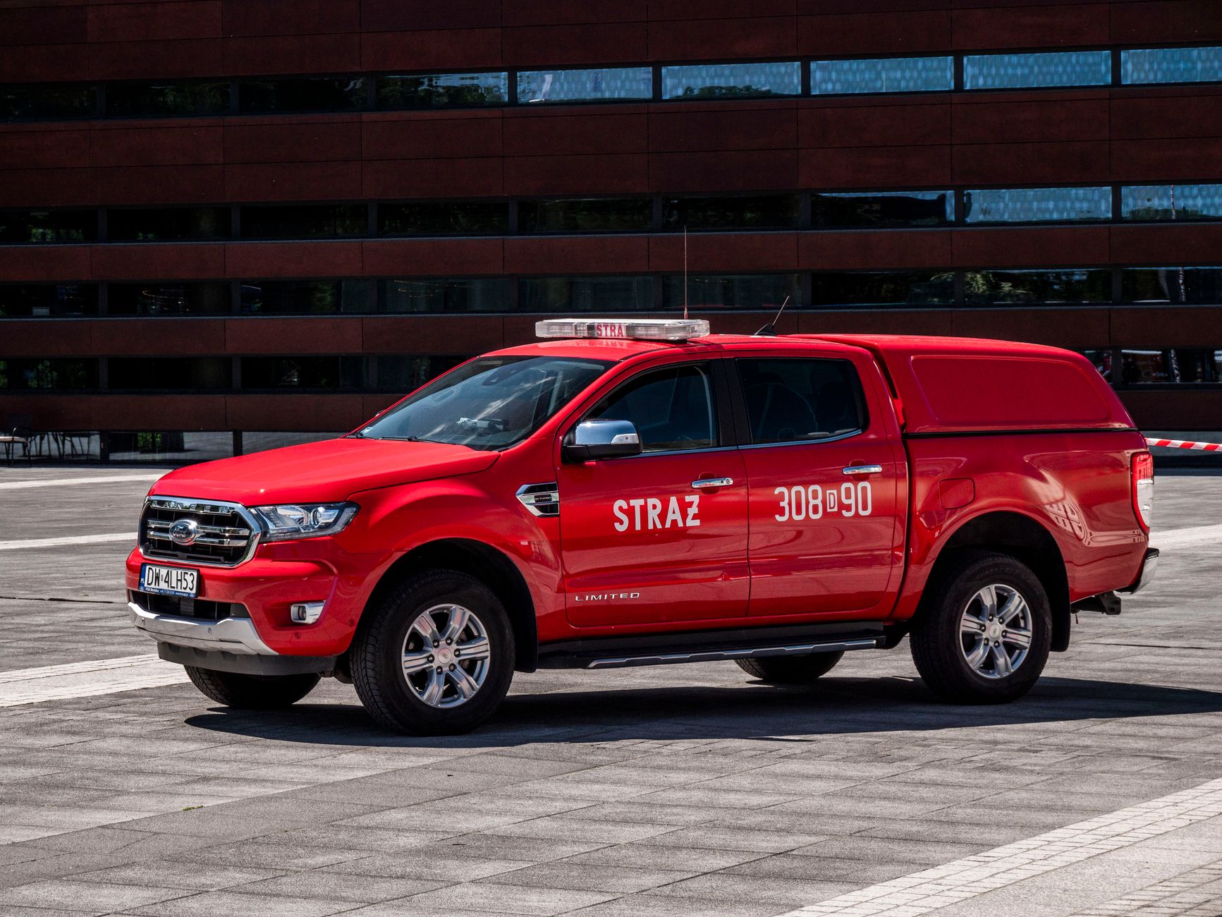 Red fire brigade truck parked in front of a modern urban building on a sunny day.