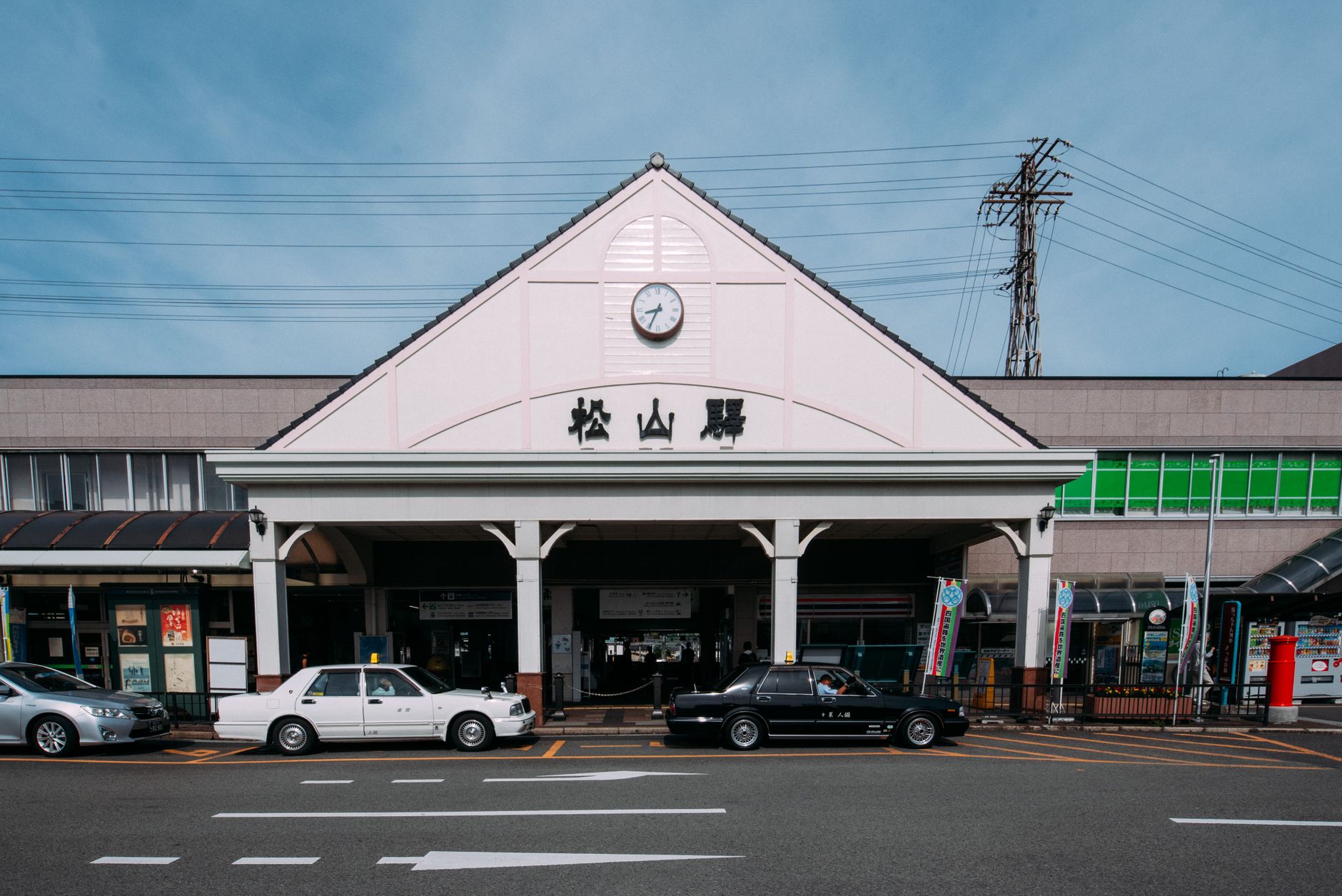 Front façade of Matsuyama Station with taxis parked outside on a clear day.
