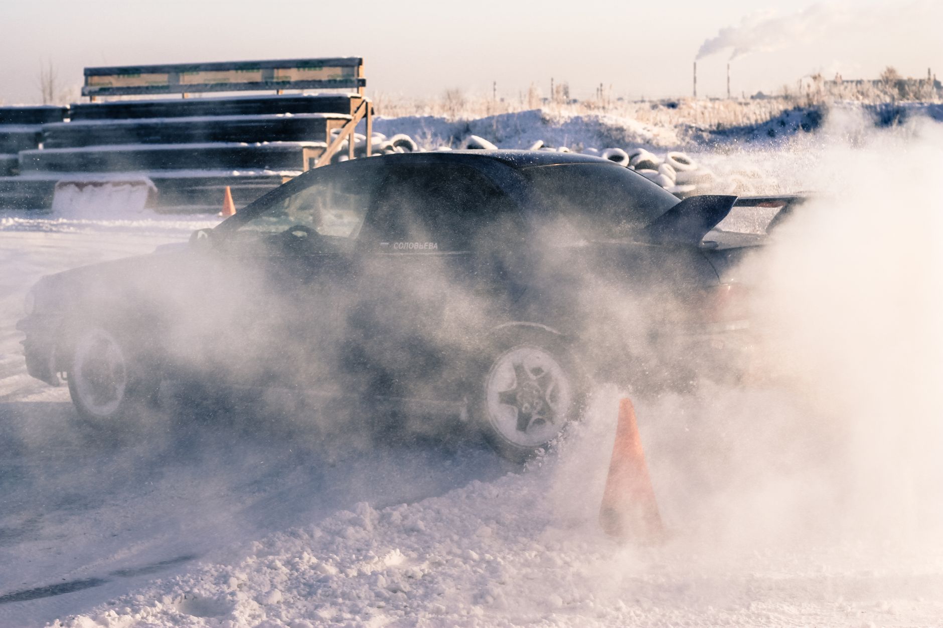 Car drifting on a snowy racetrack in Saint Petersburg, leaving a trail of smoke and snow.
