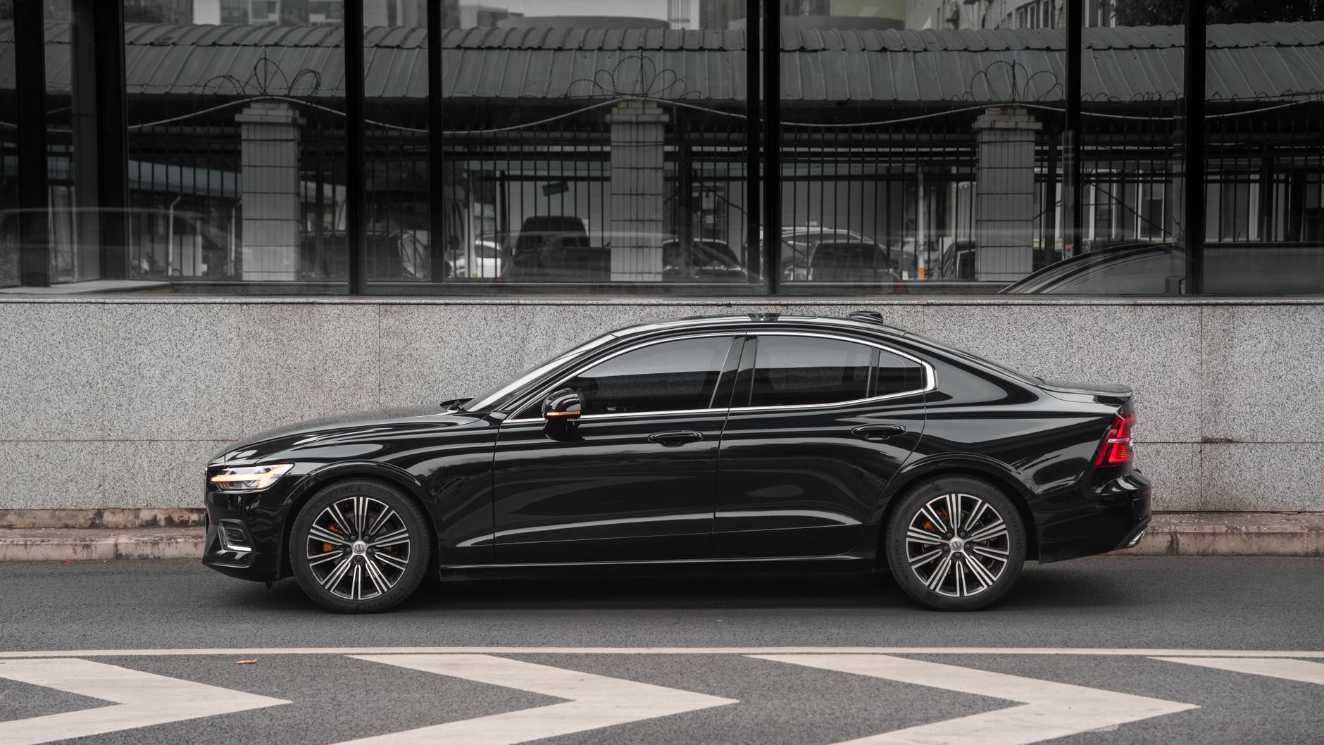 Side view of a modern black sedan parked against a city wall.