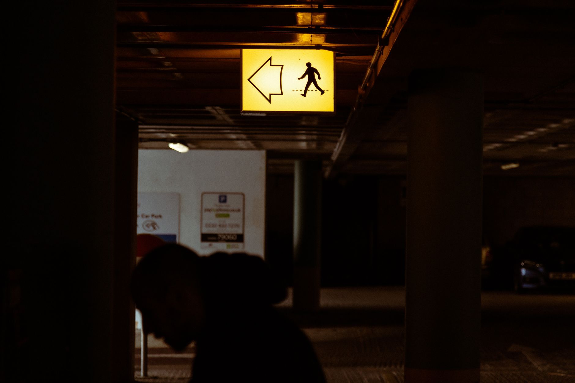 Dark parking garage scene with a glowing pedestrian arrow sign guiding the way.