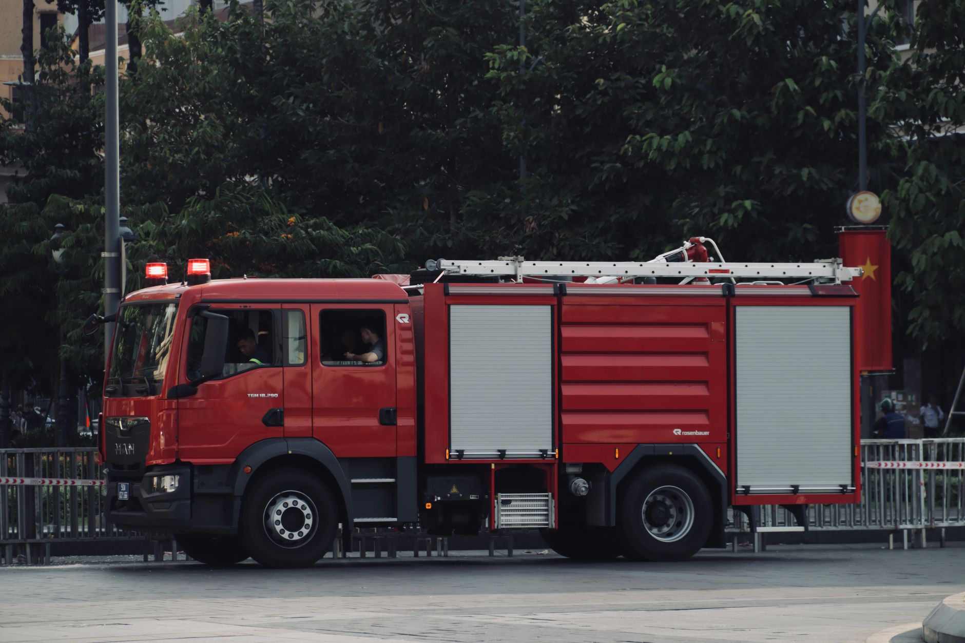 A vibrant red fire truck is parked on a city street surrounded by trees, showcasing urban emergency readiness.
