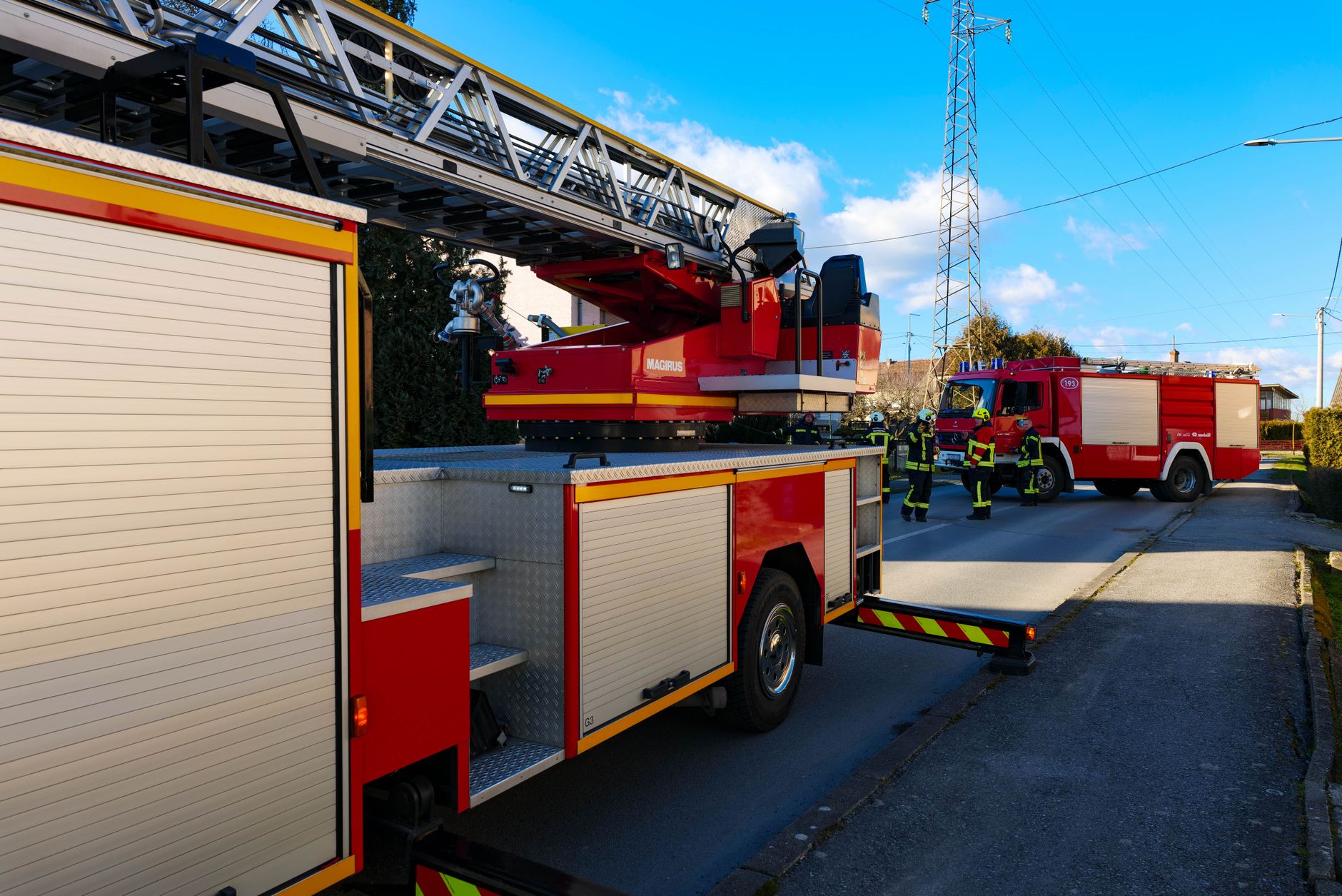 Firefighters and firetrucks in action on a city street under clear blue skies.