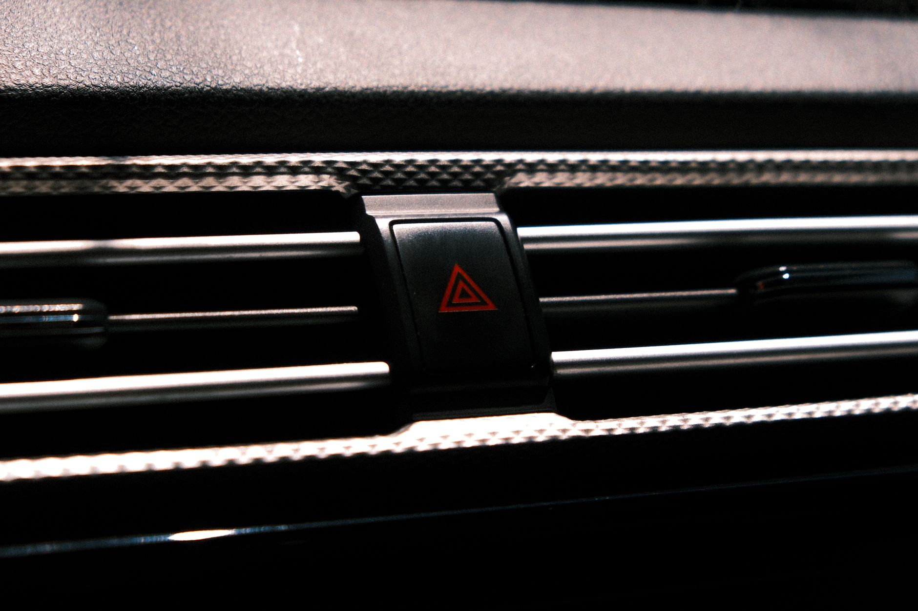 Close-up image of a car hazard light button on a dark dashboard.
