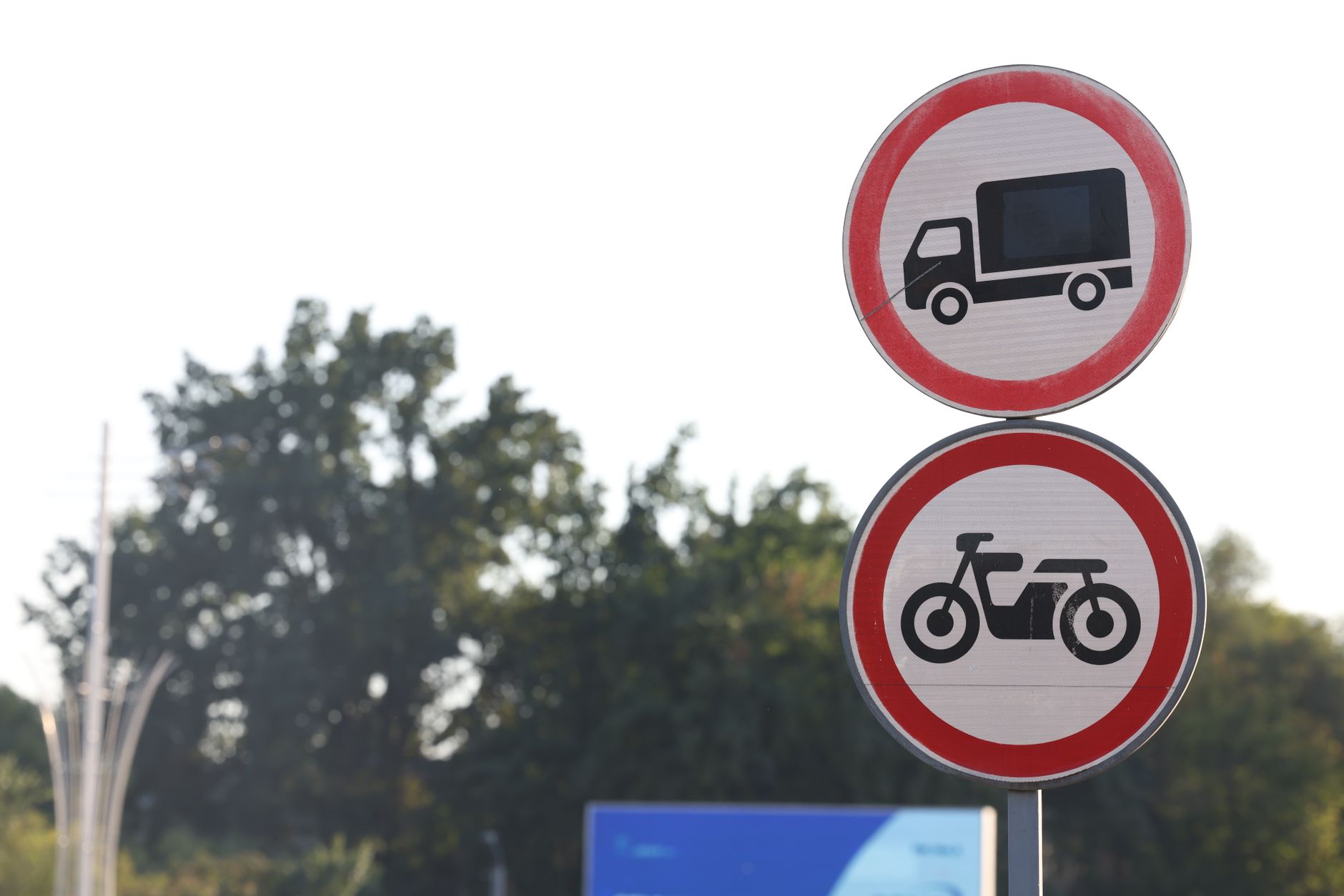Traffic signs against a backdrop of trees in Uzbekistan, prohibiting trucks and motorcycles.