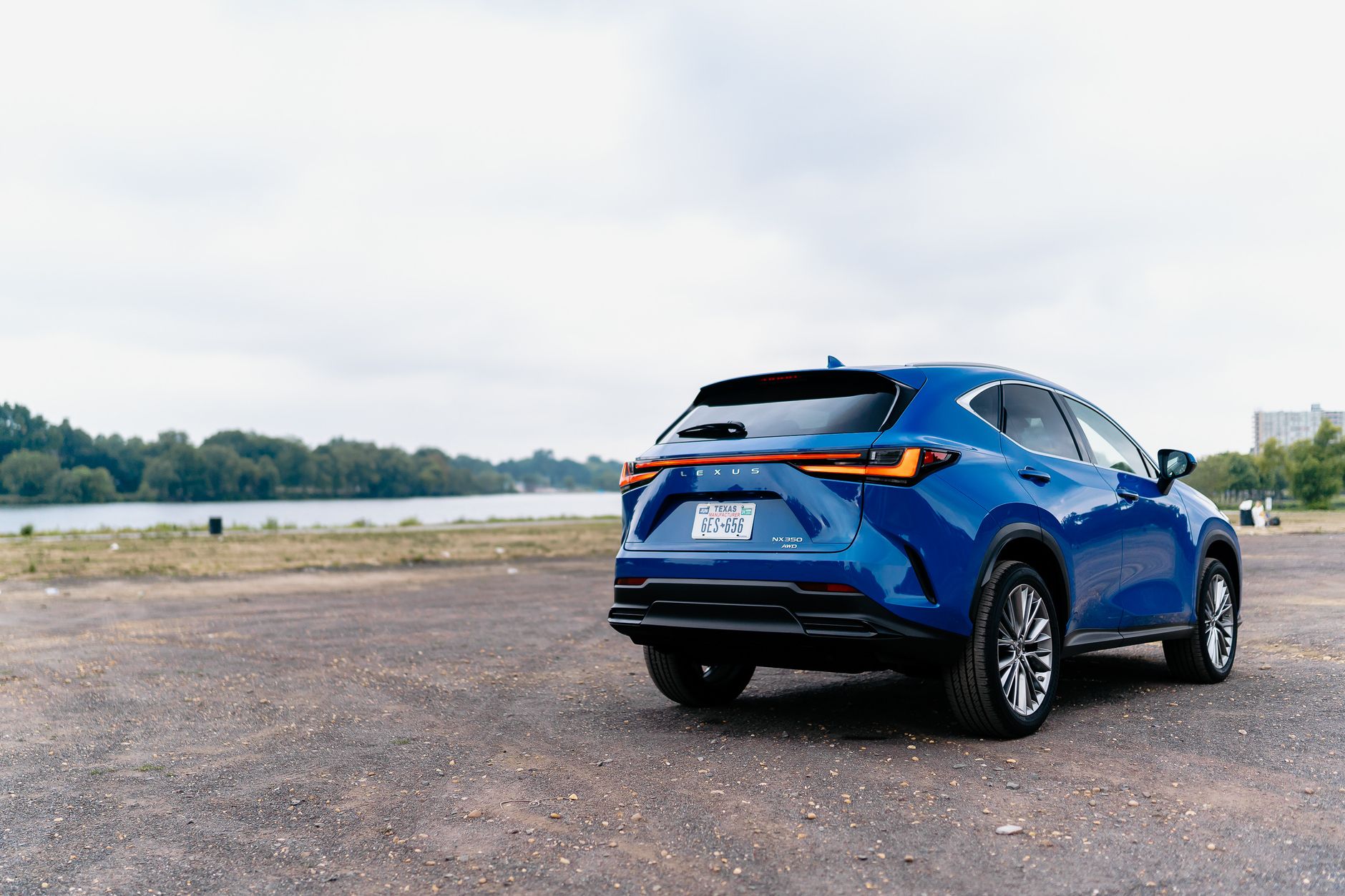 Bright blue SUV parked by a river, surrounded by lush foliage on a cloudy day.