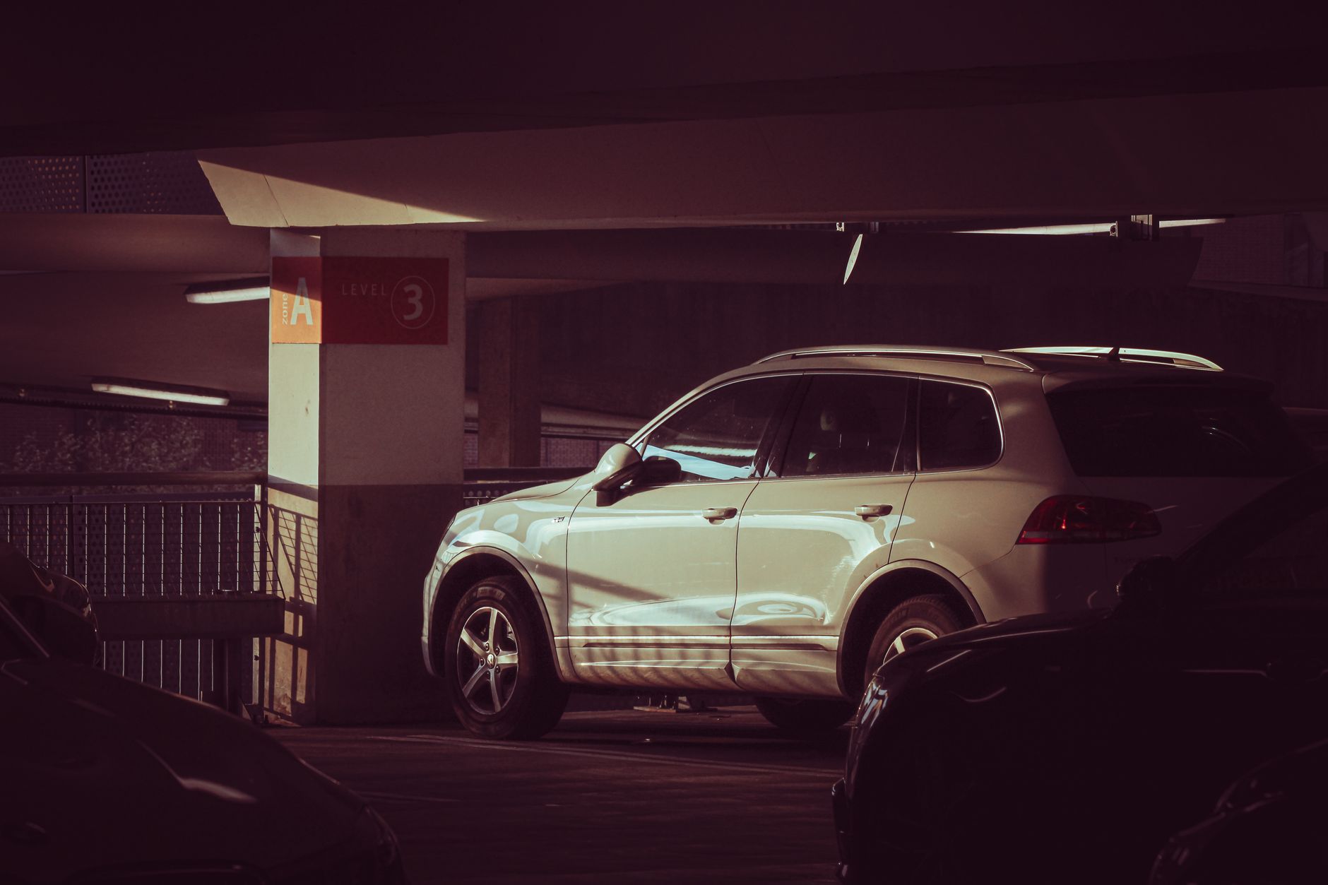 White SUV in an indoor parking garage, level 3, with dramatic lighting and shadows.