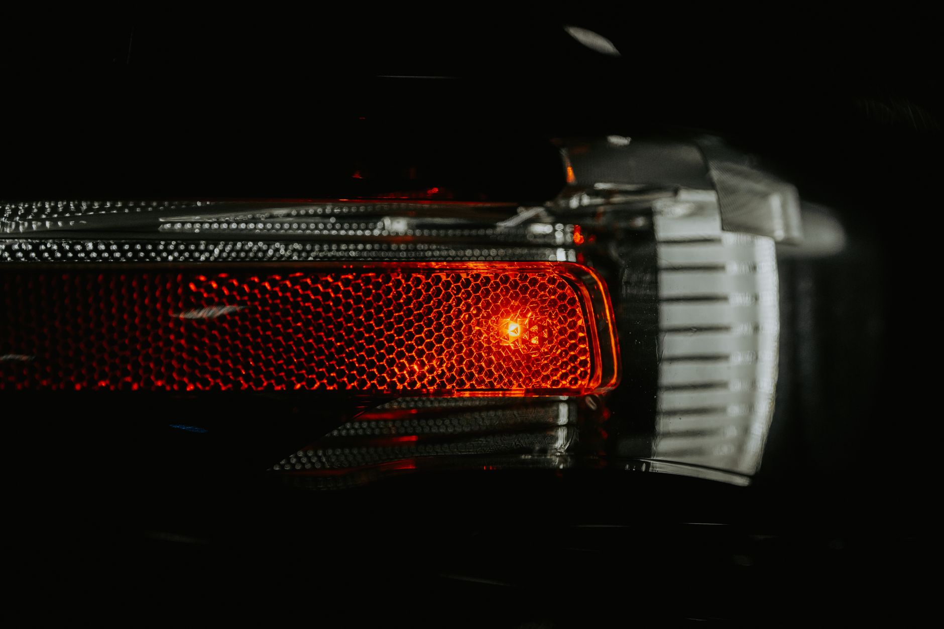 A detailed view of a car brake light with a textured lens illuminating in the dark.
