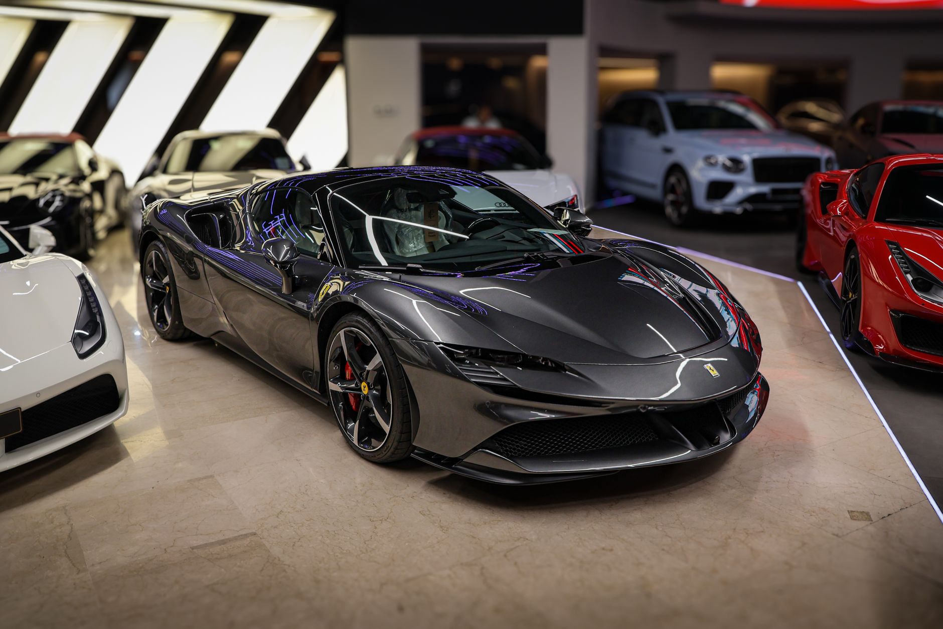 Sleek Ferrari sports car on display, surrounded by luxury vehicles in an indoor showroom.