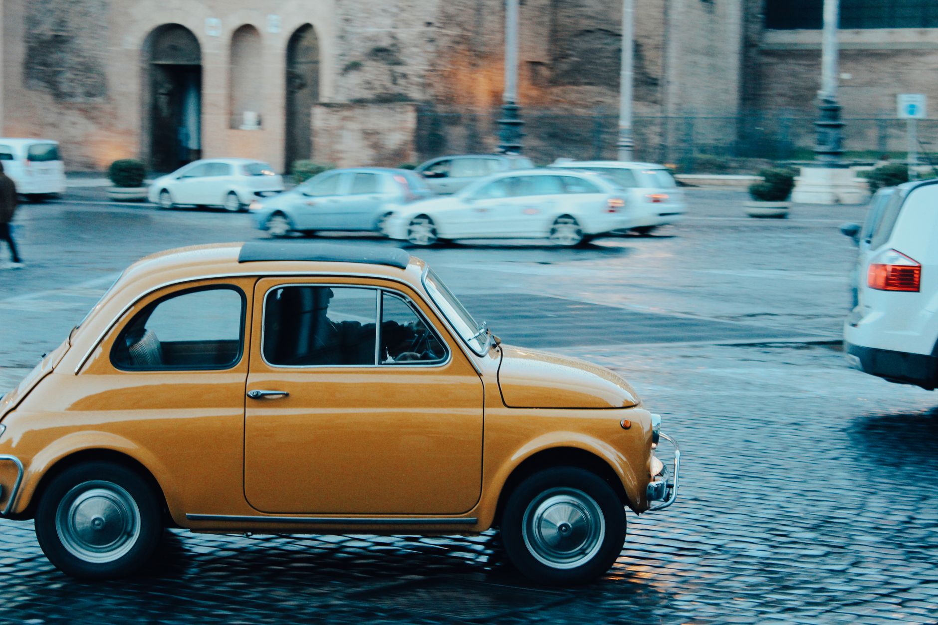 Yellow vintage Fiat 500 driving through the cobblestone streets of Rome, Italy.
