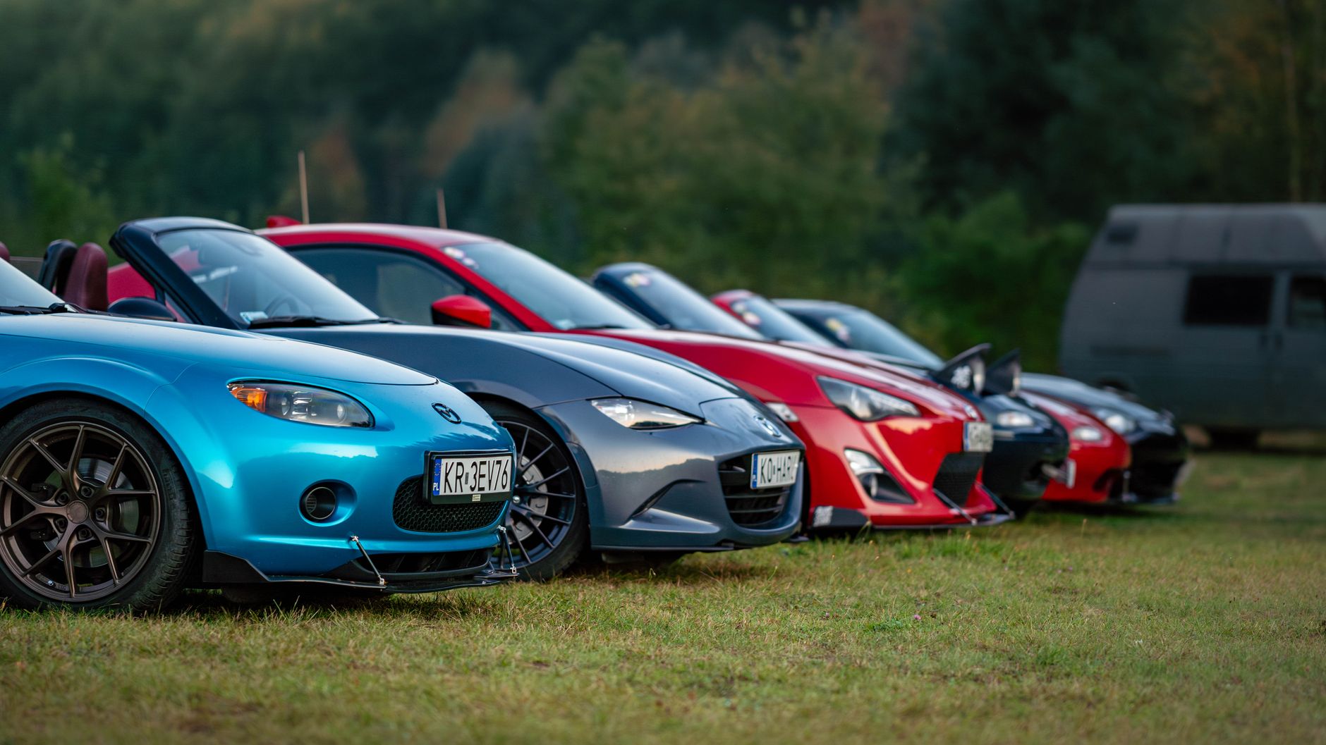 A lineup of colorful sports cars parked on grassy terrain outdoors during the day.
