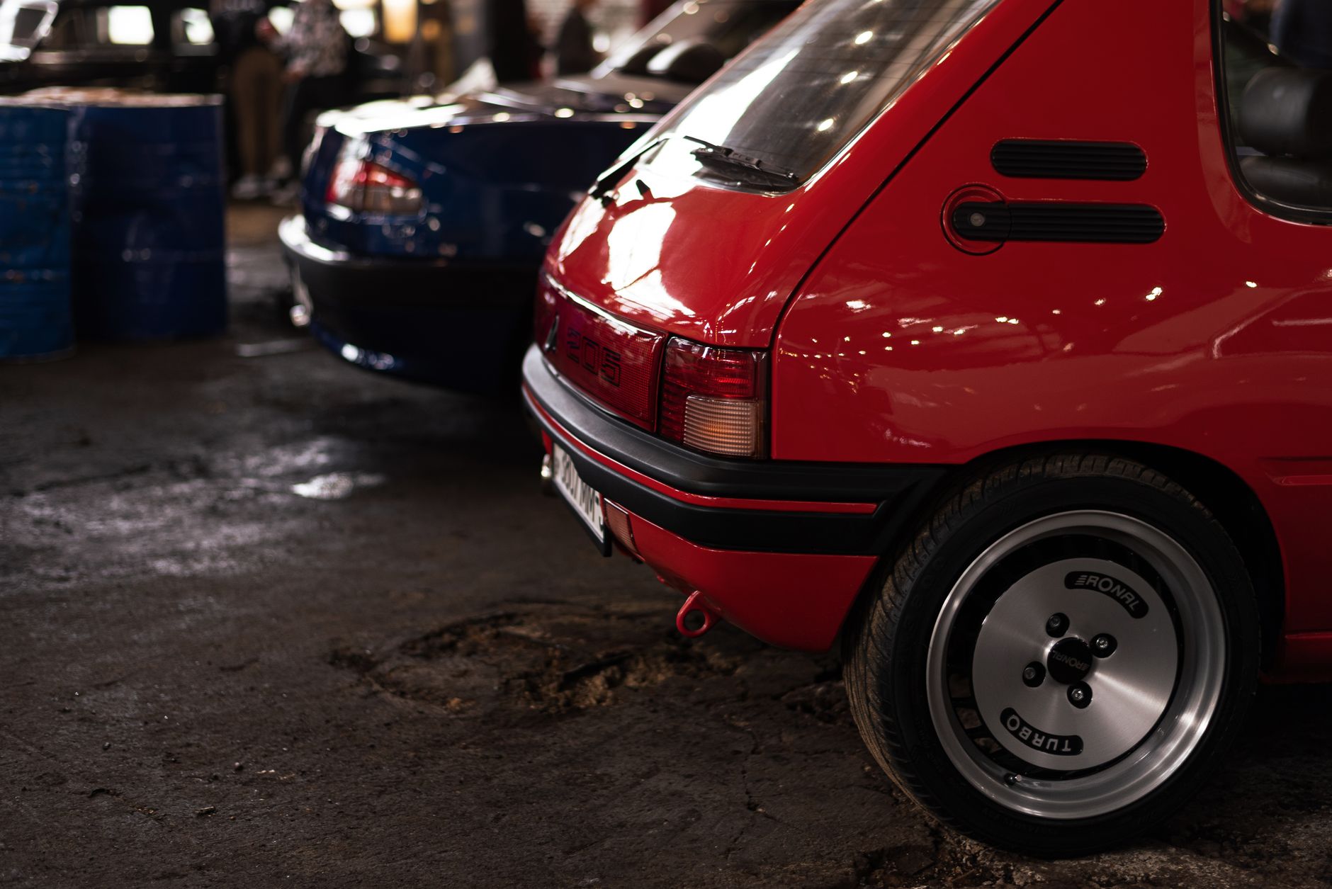 A vibrant red Peugeot 205 hatchback captured in a dimly lit urban environment.