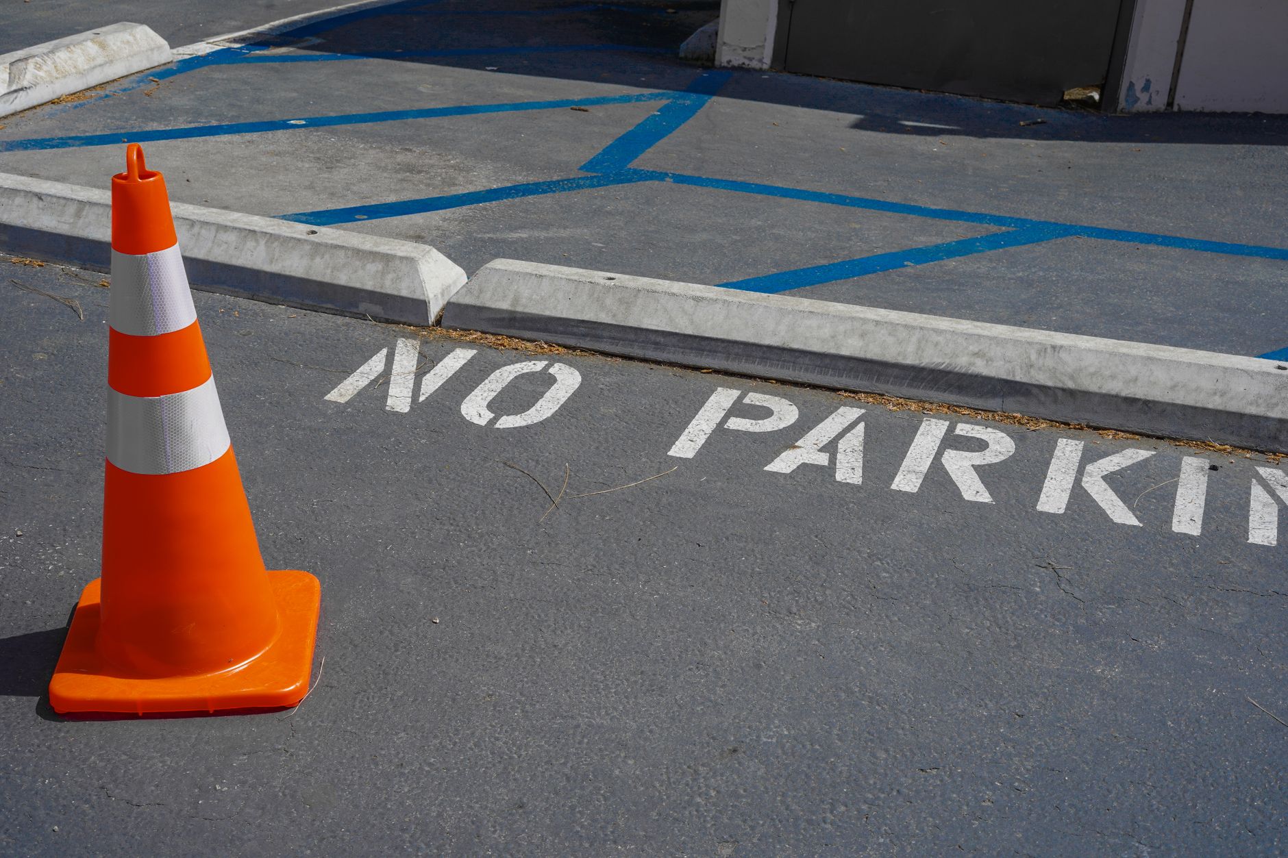 An orange traffic cone on a no parking zone with blue lines in a city street.