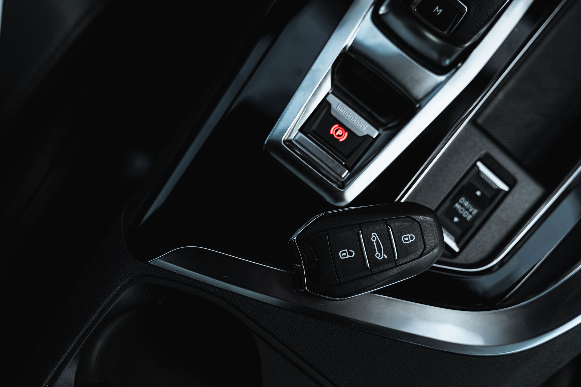 Close-up view of a keyless fob and electronic handbrake in a modern car interior.