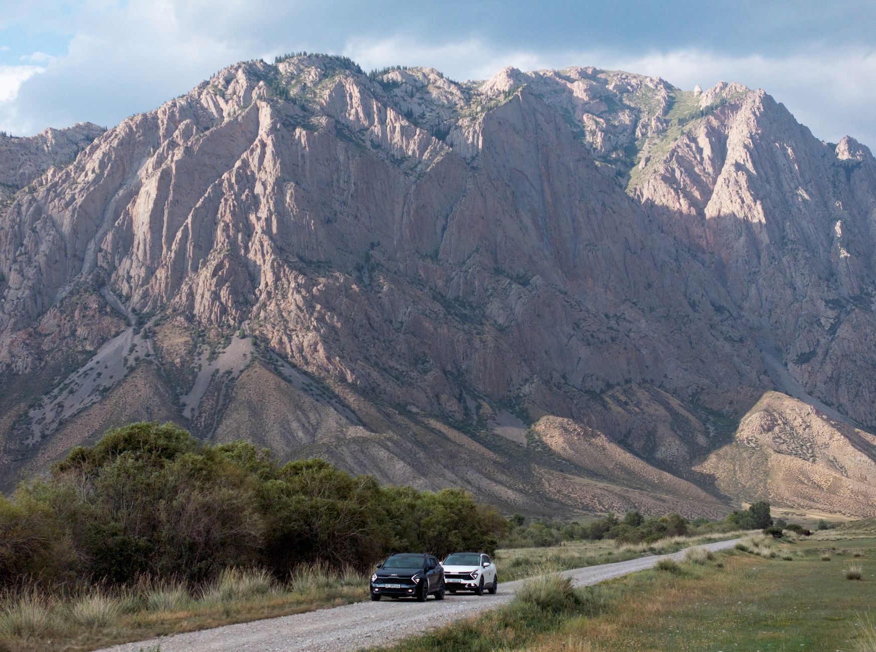 Two SUVs driving on a remote road with stunning mountain scenery in Kyrgyzstan.