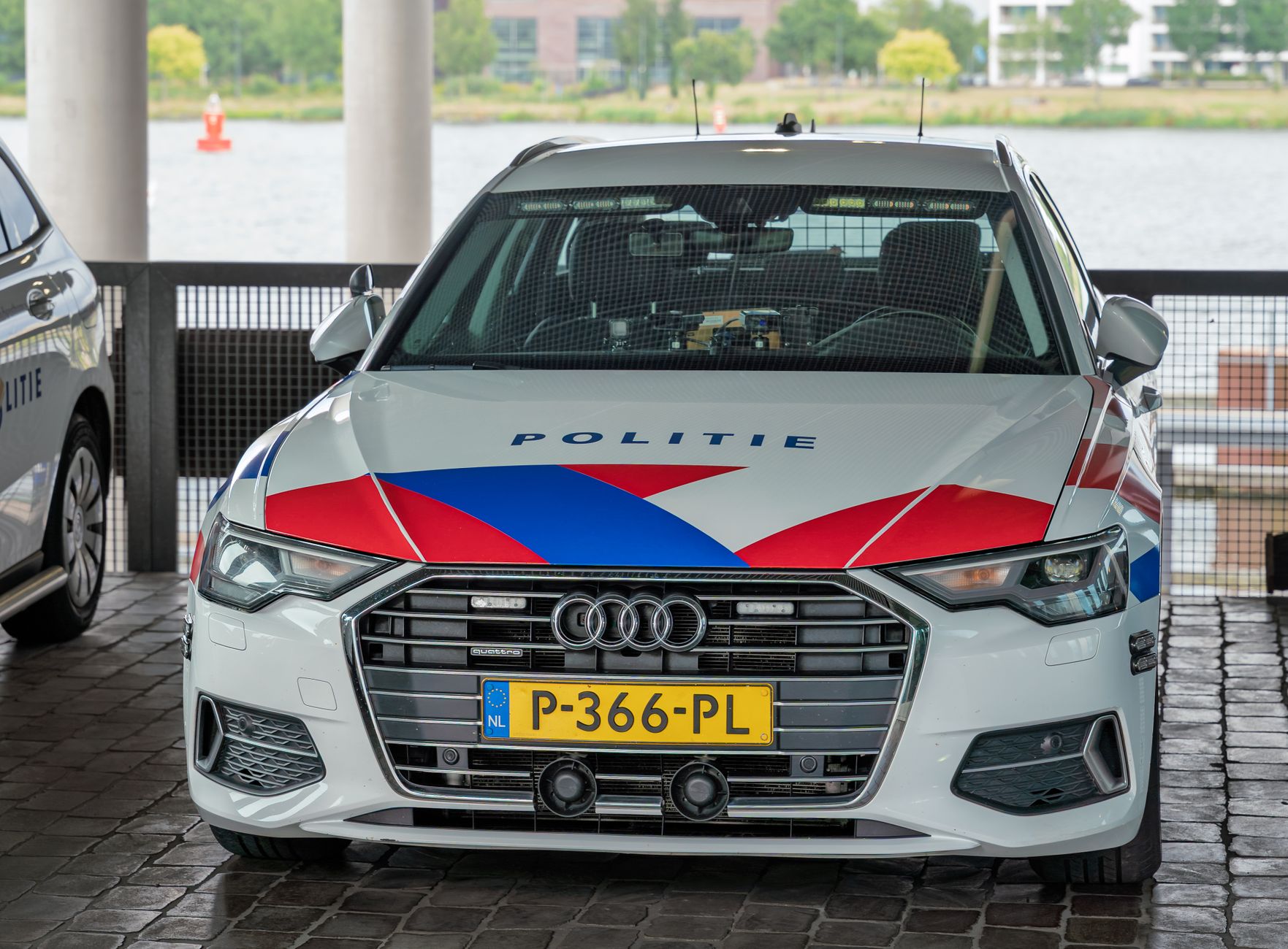 A Dutch police car with 'Politie' markings parked in an urban environment, displaying its distinctive red, white, and blue colors.