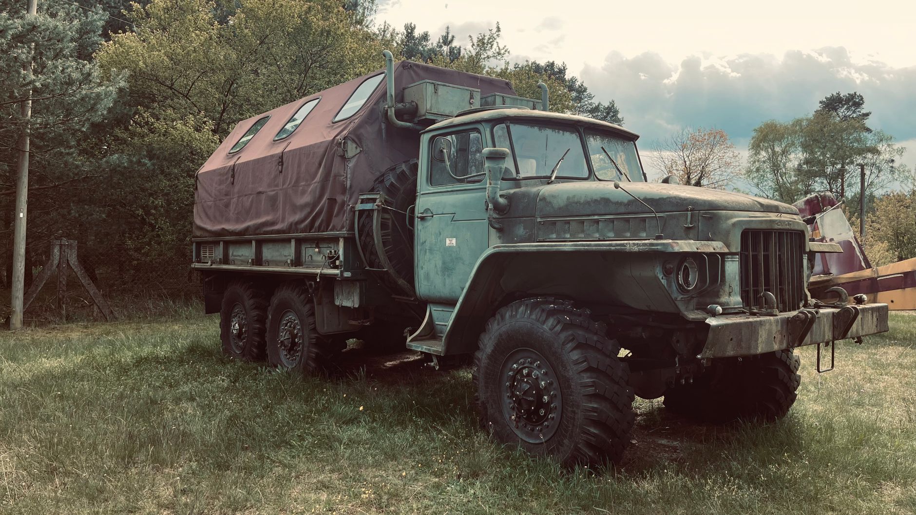 An old army truck with a covered back parked outdoors, surrounded by trees.