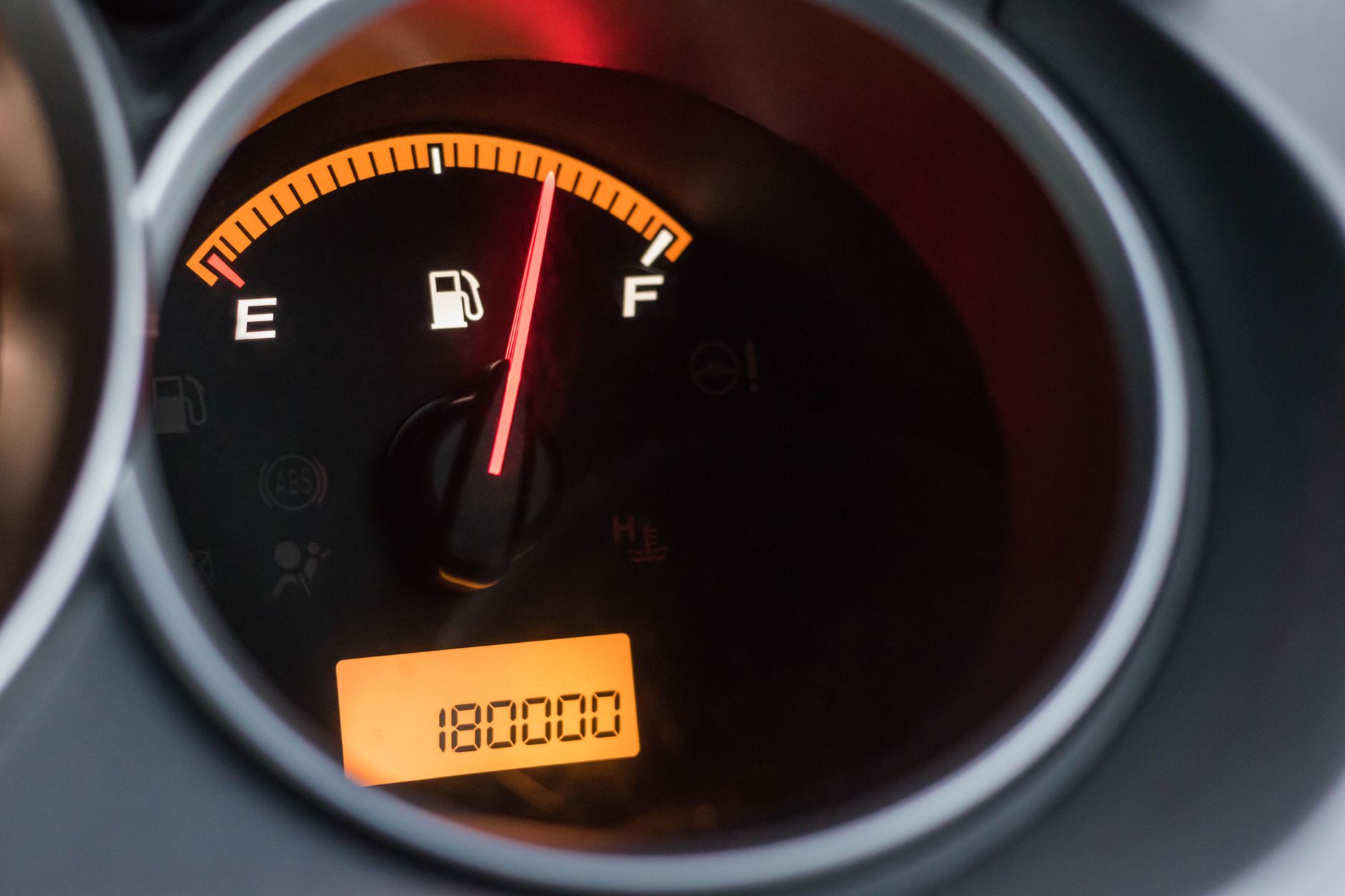 Close-up image of a car's fuel gauge showing a full tank with an odometer reading of 180000 miles.