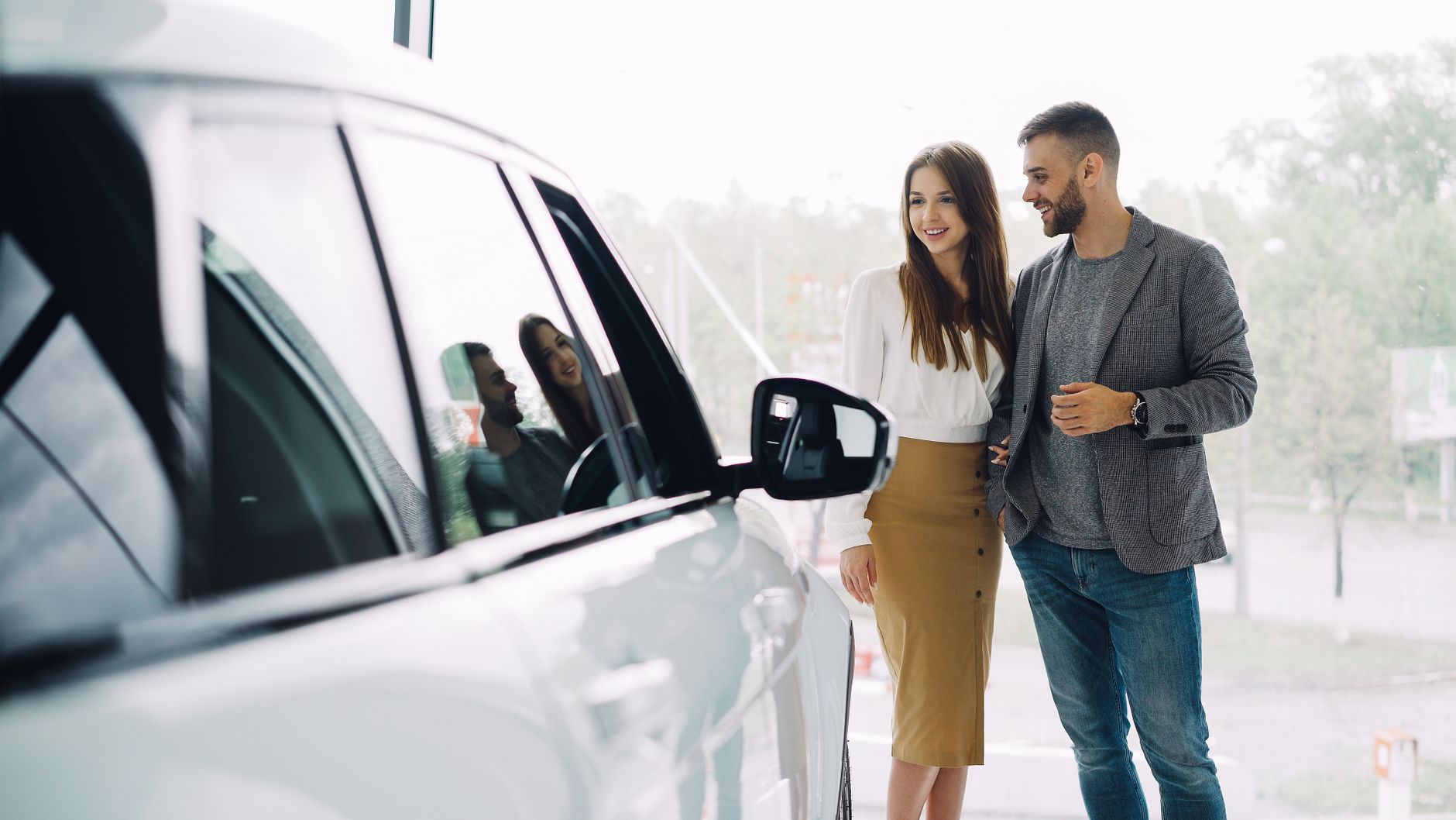 Smiling couple exploring a new car at a dealership, excited about their purchase.