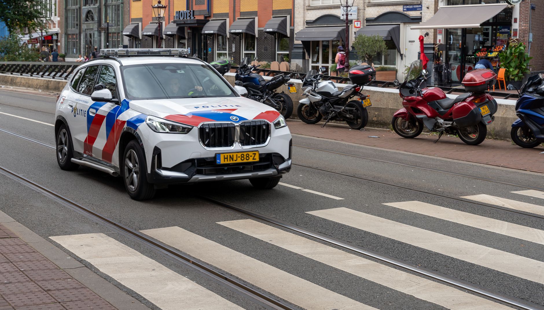 Dutch police car driving through an urban street in Amsterdam with motorcycles parked nearby.