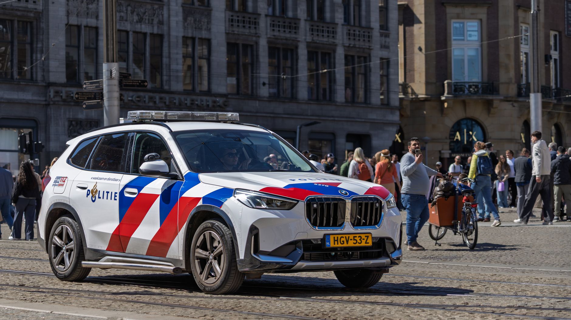 Dutch police SUV patrols in a busy city square, capturing urban life and public safety.