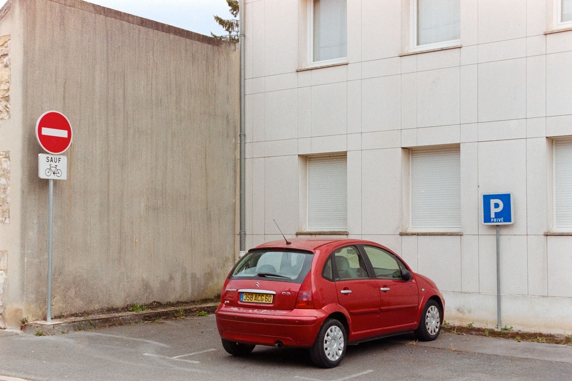 Red car in private parking near building facade, Compiègne, France.
