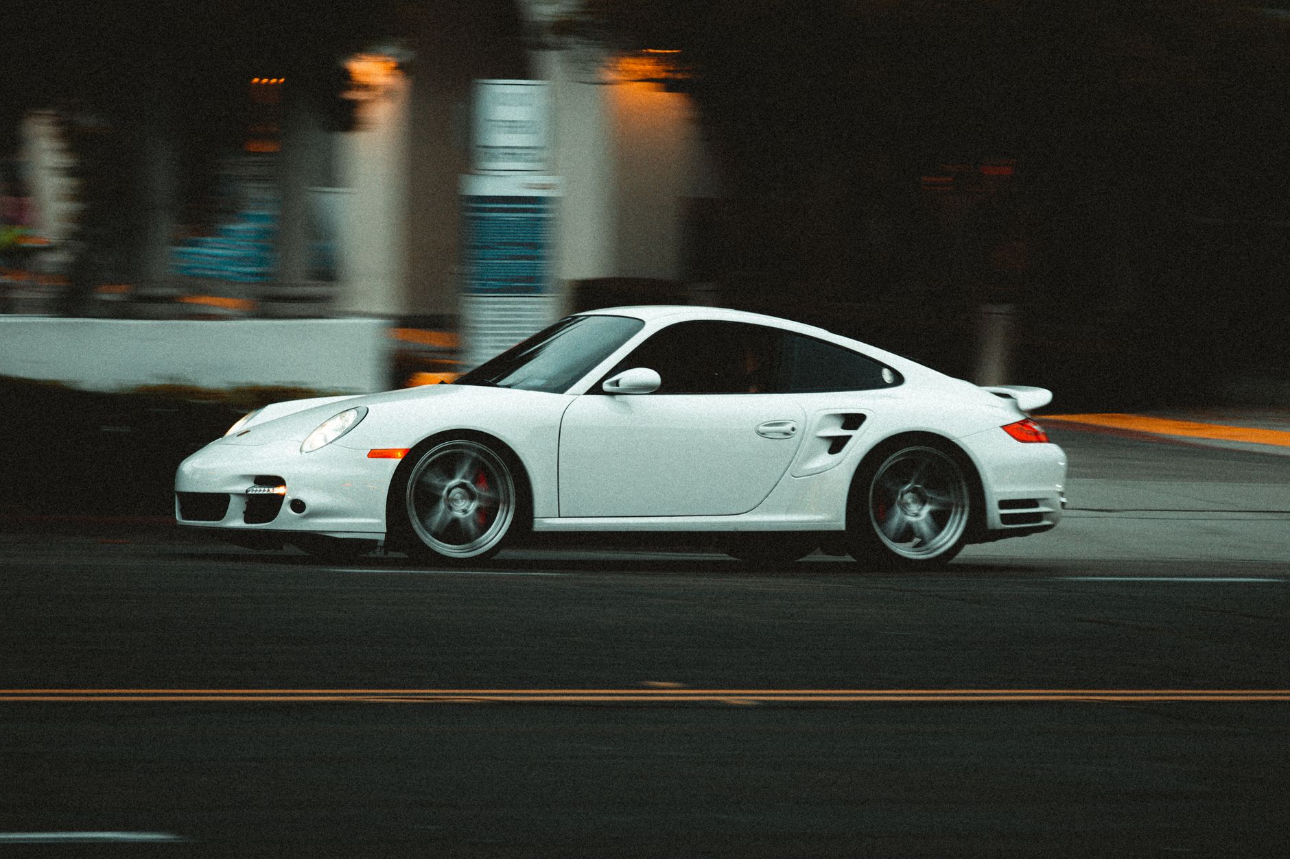Dynamic shot of a white Porsche in motion on a San Diego street at dusk, capturing speed and elegance.