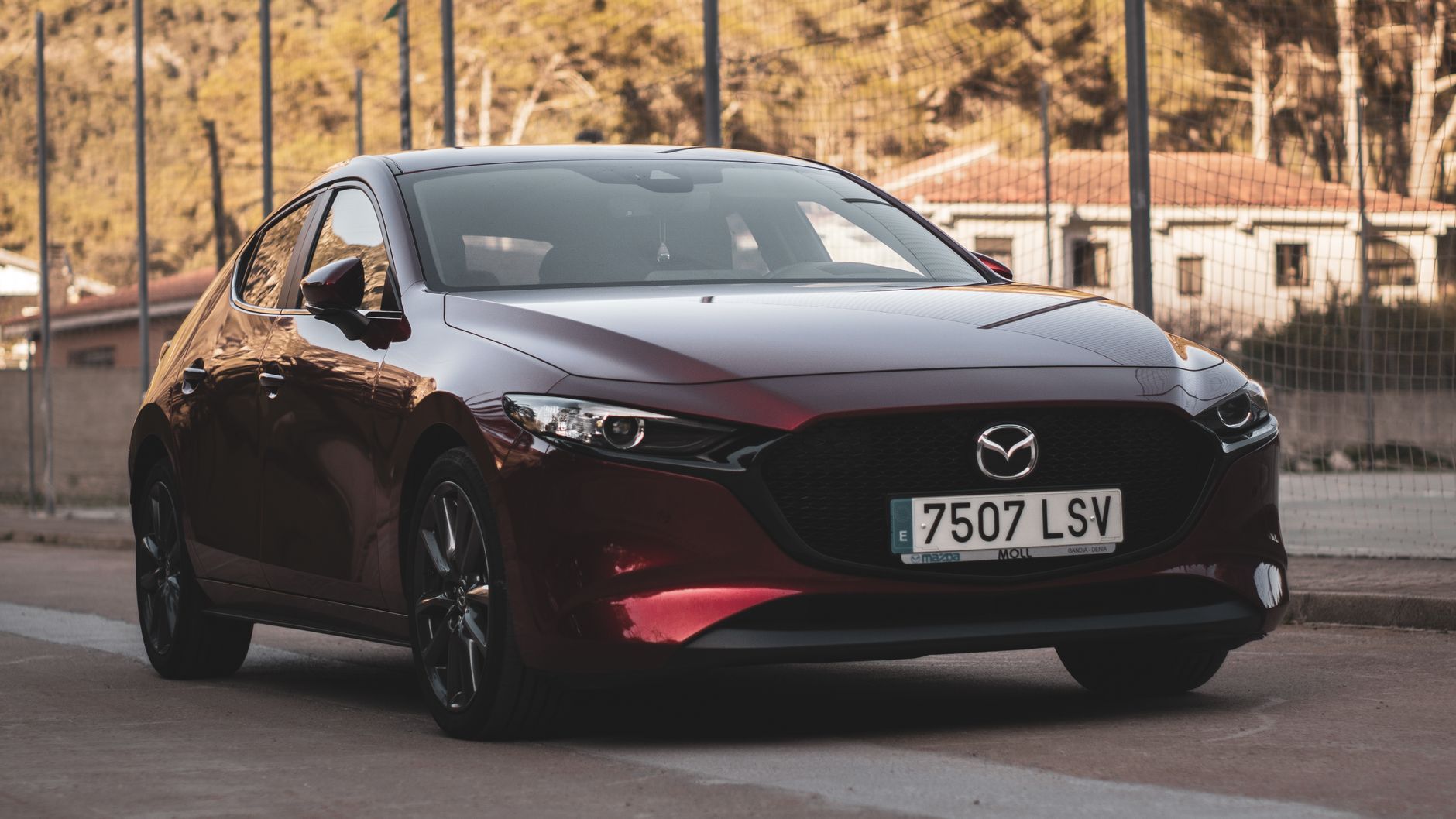 Stylish red Mazda car parked on an urban street with trees and sunlight in the background.