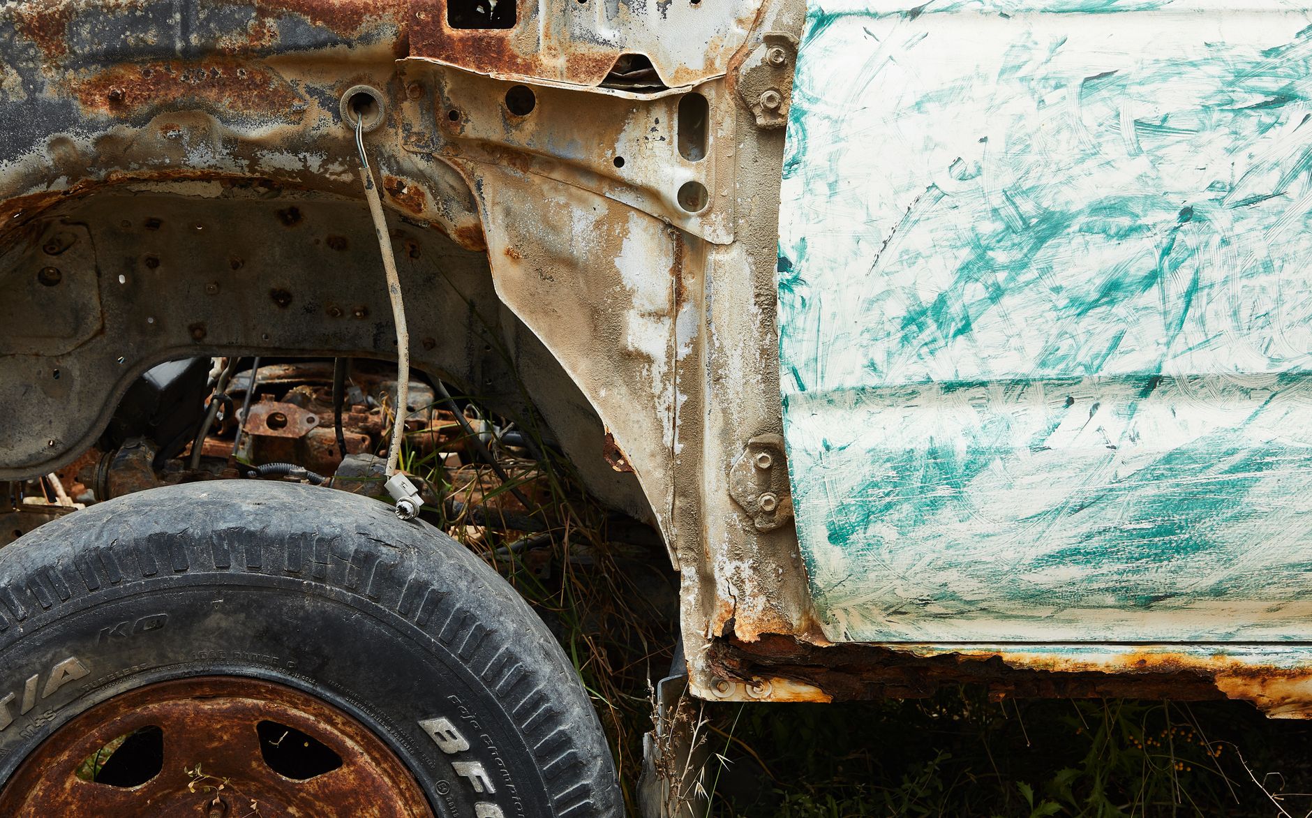 Old iron damaged automobile covered with rust and corrosion in field in daytime