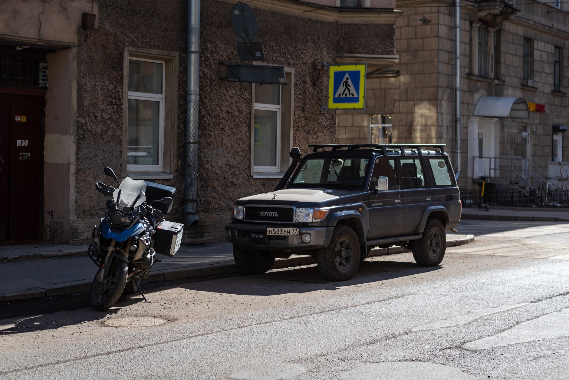 Parked SUV and motorcycle on a city street with a pedestrian crossing sign.