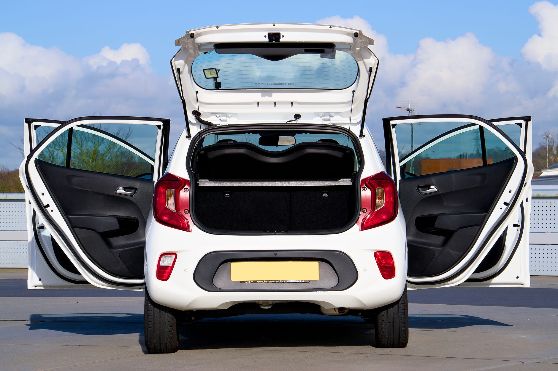 A white Kia Picanto displayed with all doors open from the rear view in Harlow, England.