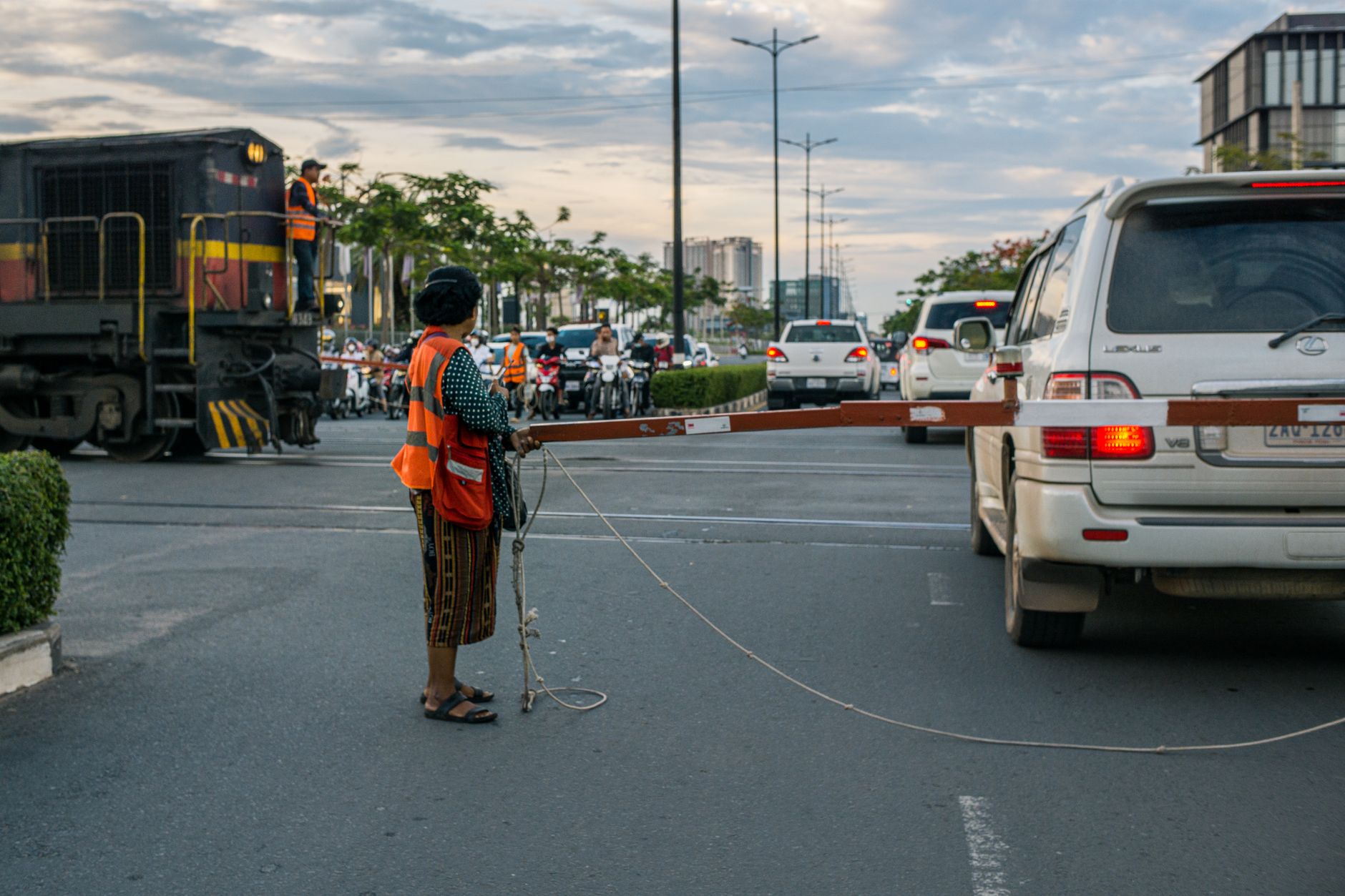 A woman in a reflective vest manages traffic at a level crossing with an approaching train.