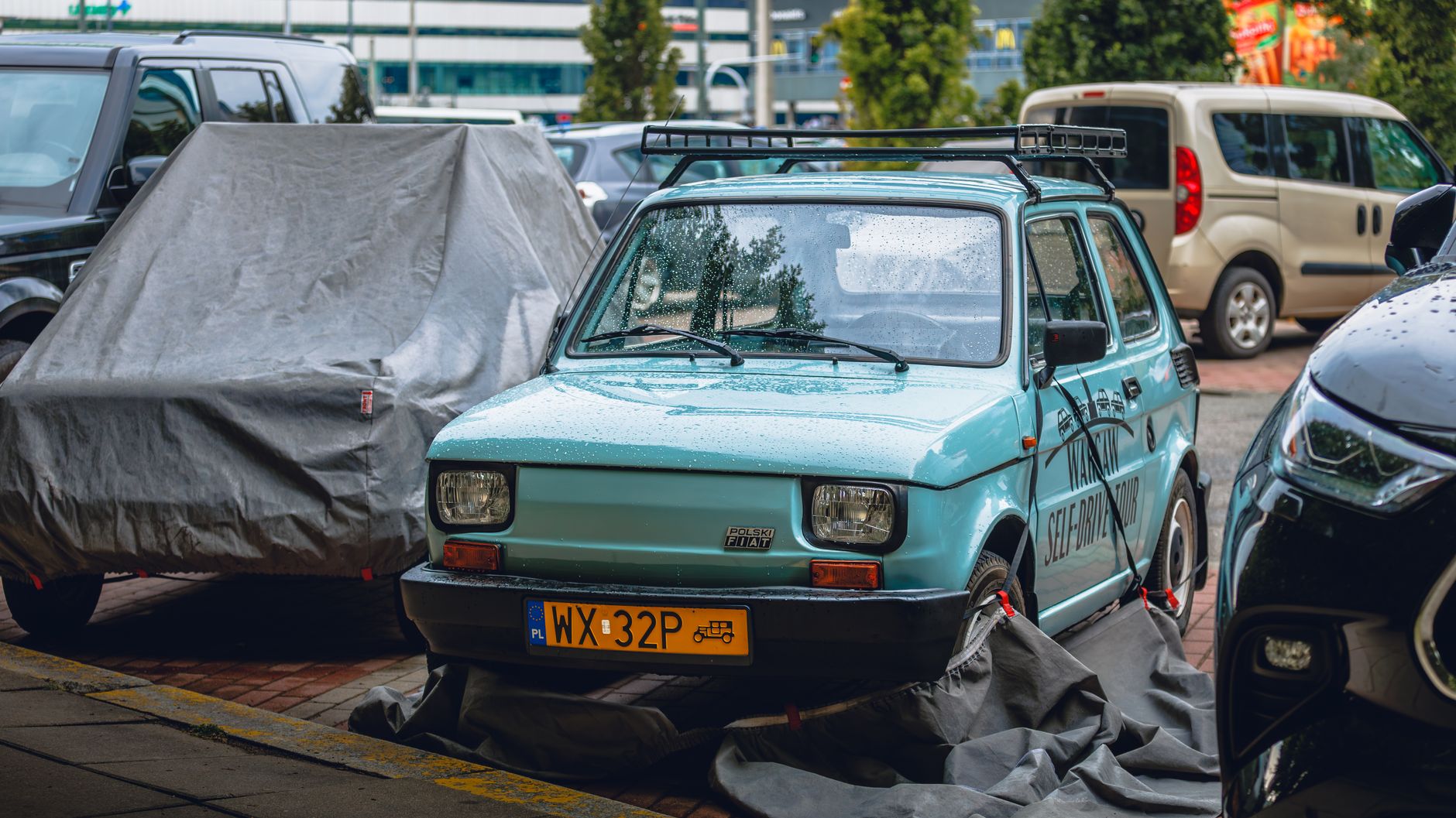 Vintage Fiat 126p spotted on a rainy day, parked among modern vehicles.