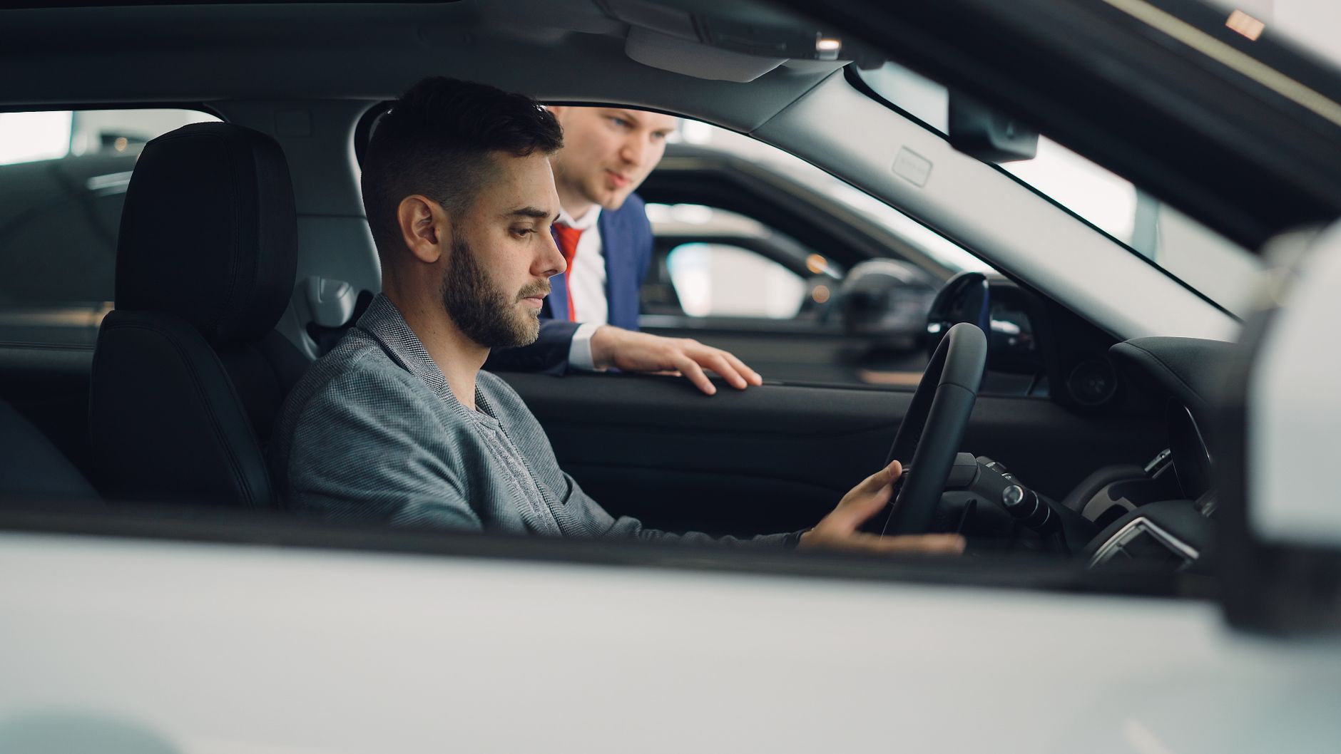 Man examining car interior with salesman at a dealership, highlighting car features.