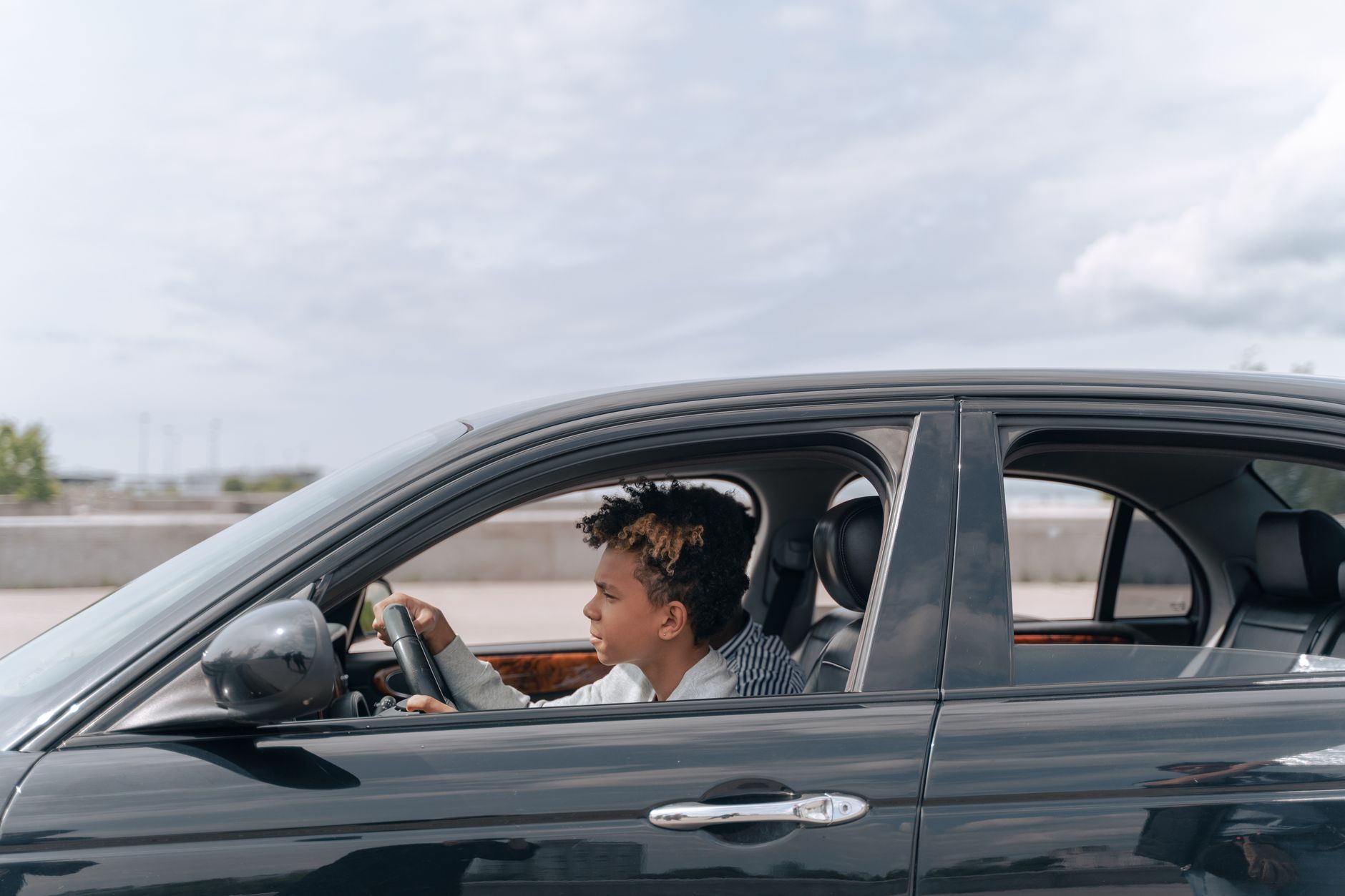 Side view of a young male teenager focused on driving a car in bright daylight.