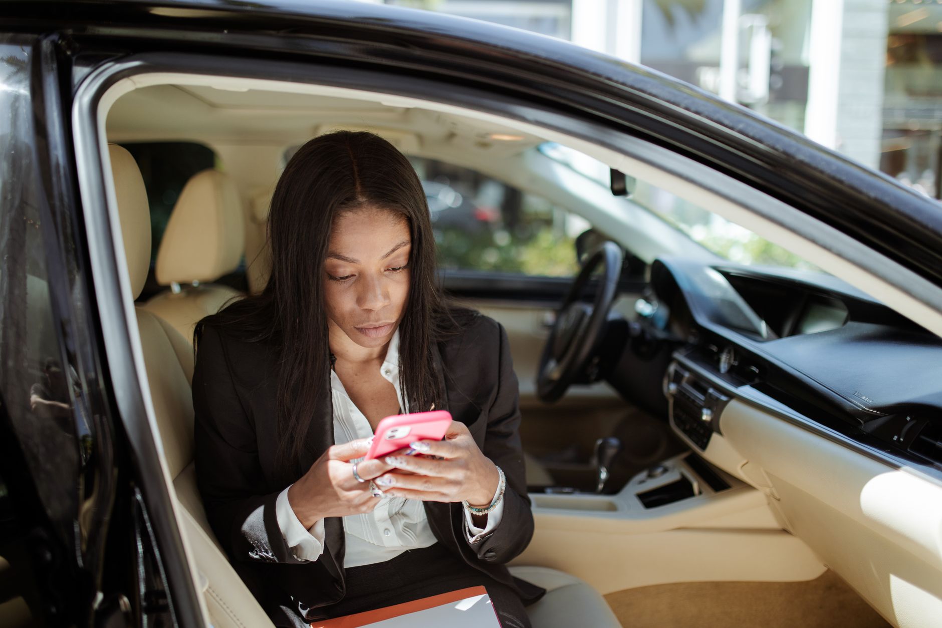A businesswoman uses her smartphone while seated in a car, focusing intently on the screen.