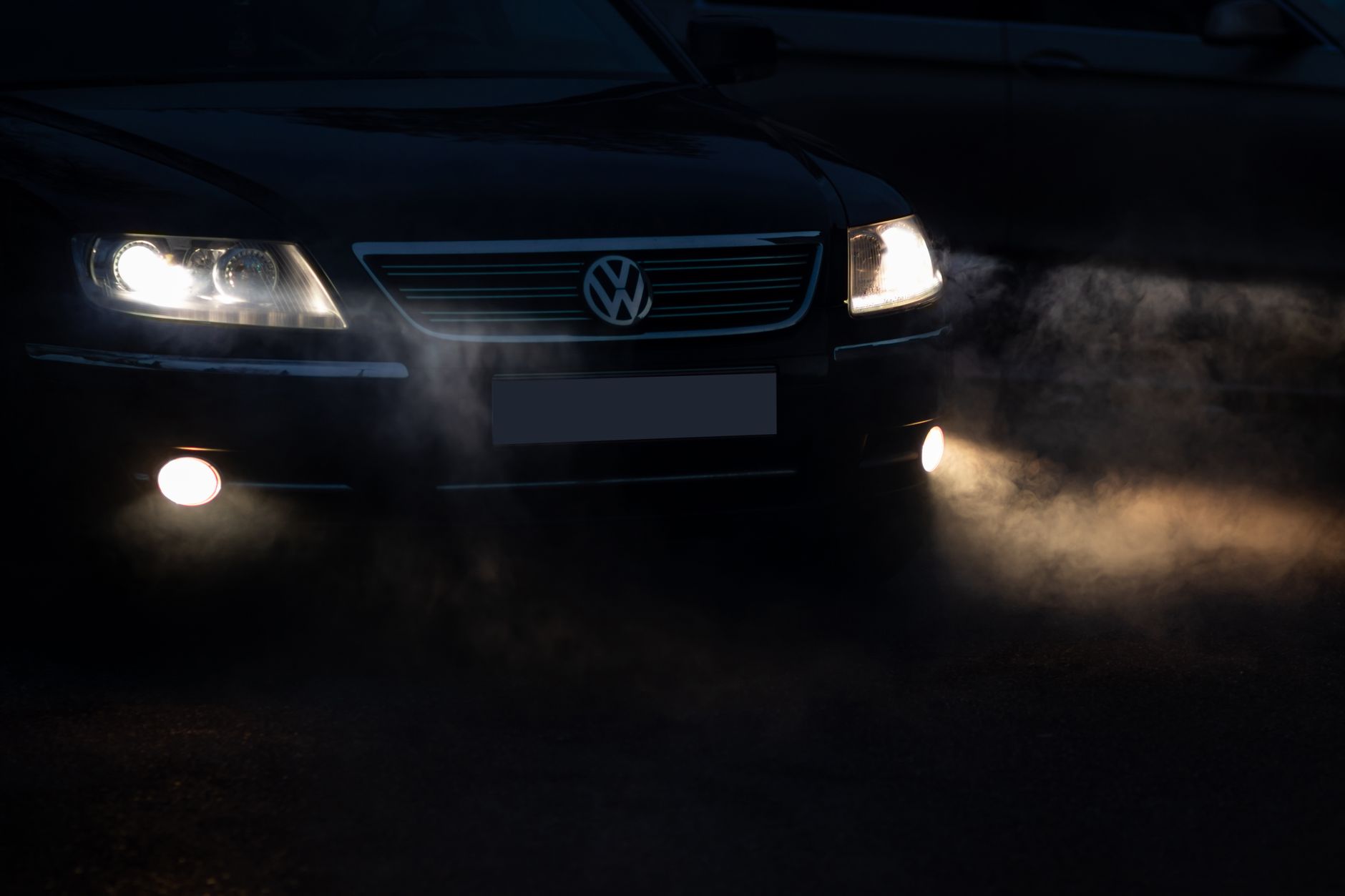 A close-up view of a car's headlights cutting through the night fog, creating a moody and mysterious atmosphere.