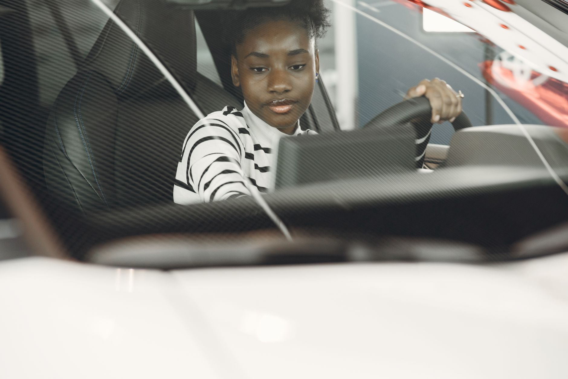 Young woman with black hair driving a car, captured from the interior with focus on the steering wheel.
