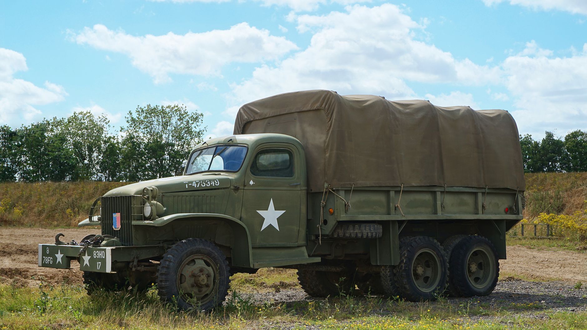 A classic green military truck with a canopy parked in a rural field under a blue sky.
